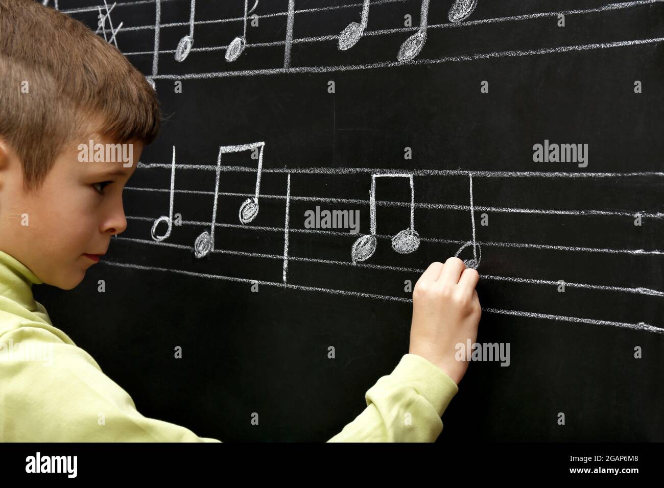 Boy Opening Note Cute boy writing at the blackboard with musical notes, in the classroom ...