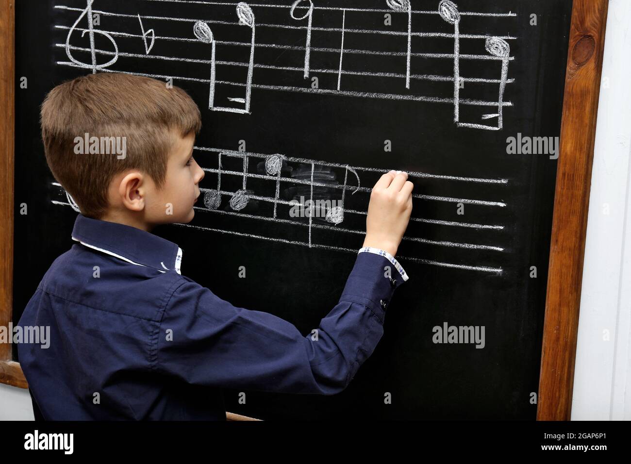 Boy Opening Note Cute boy writing at the blackboard with musical notes, in the classroom ...