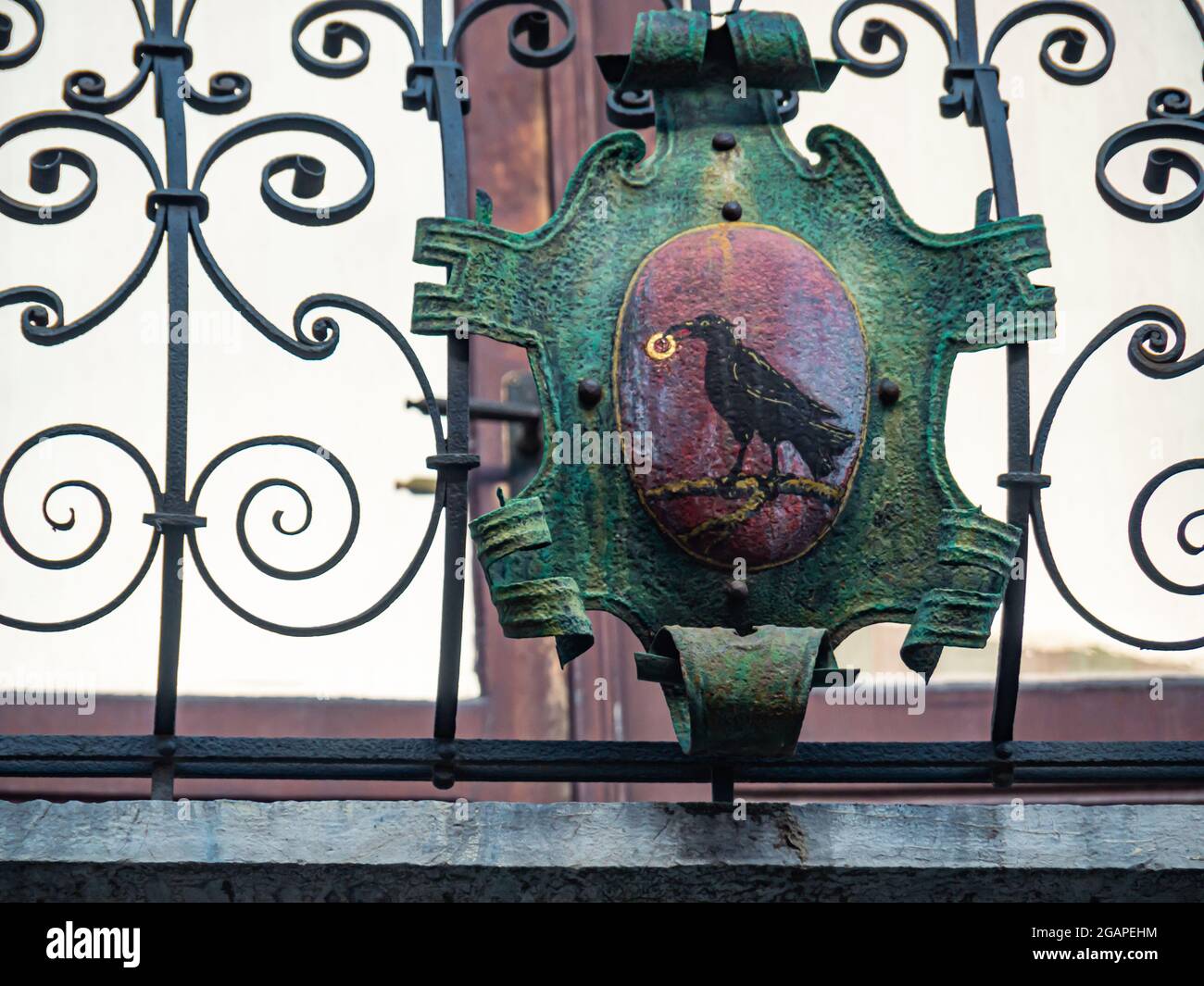 A rusty old gate with a heraldic shield displaying a raven holding a golden ring on a red background Stock Photo