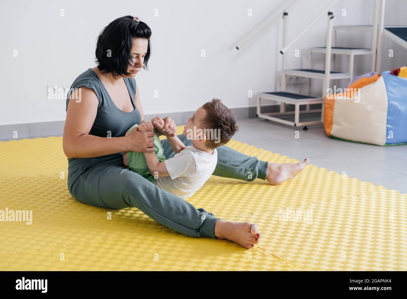 Rehabilitation of child with cerebral palsy in special center. Mother doing physical exercises and happily playing with boy, Sport activities for Stock Photo