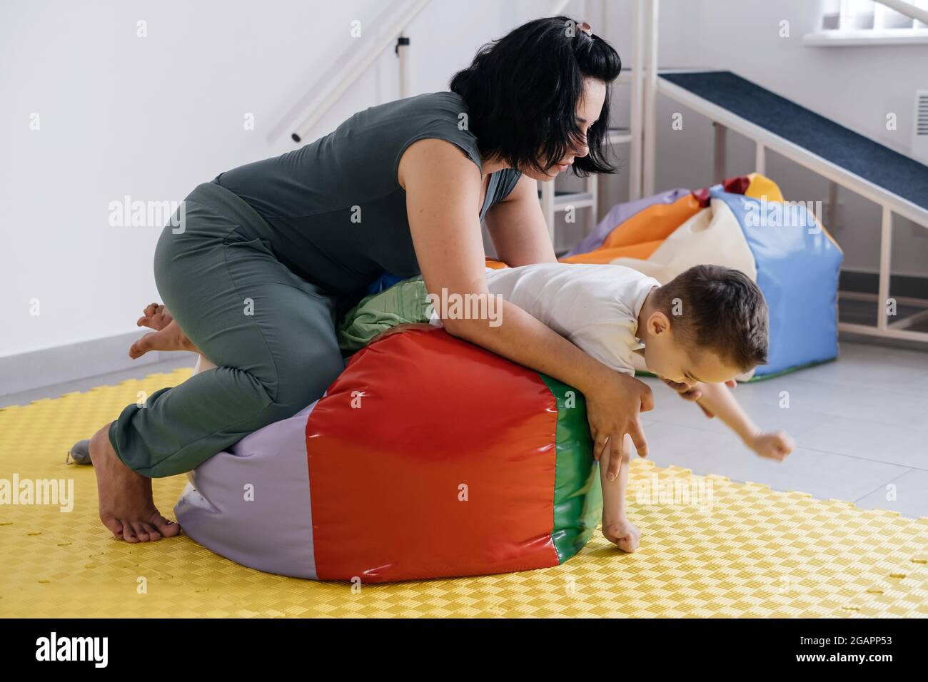 Therapist doing exercises on the mat with disabled child. Boy with