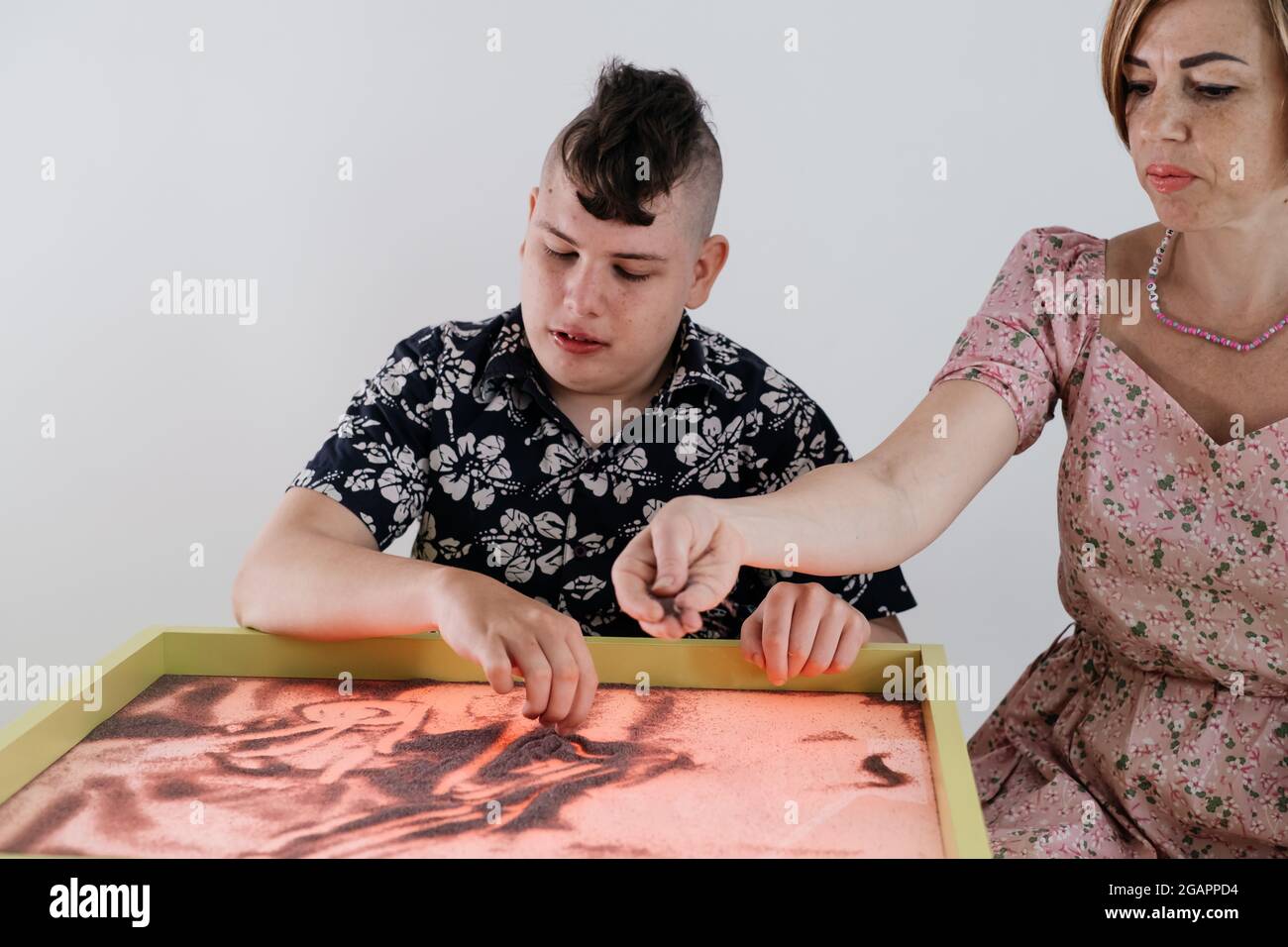 Children with disability getting sensory activity Sand tray, sand table for animation, cerebral palsy boy playing calming game, training fine motor Stock Photo