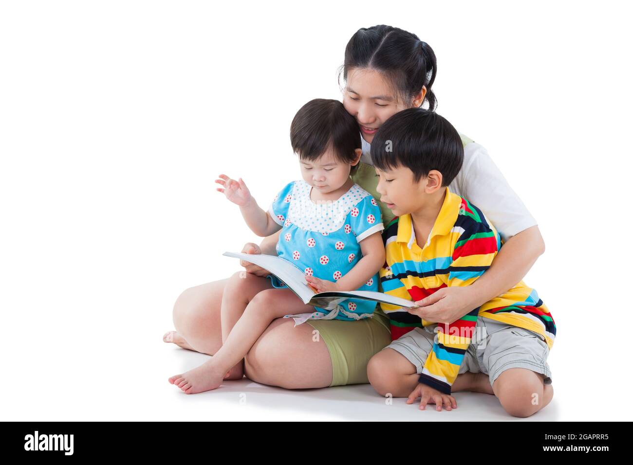 Image of cute young female with two little asian children reading a book together, daughter sitting on the lap, son sitting on the floor, happy family Stock Photo