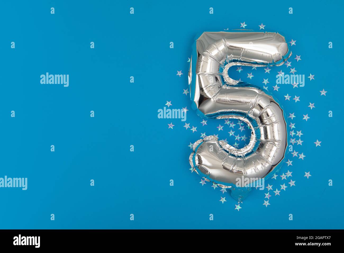 Silver balloon 5 on a blue background with confetti stars. Number five 5. Holiday Party Decoration or postcard concept with top view on blue backgroun Stock Photo