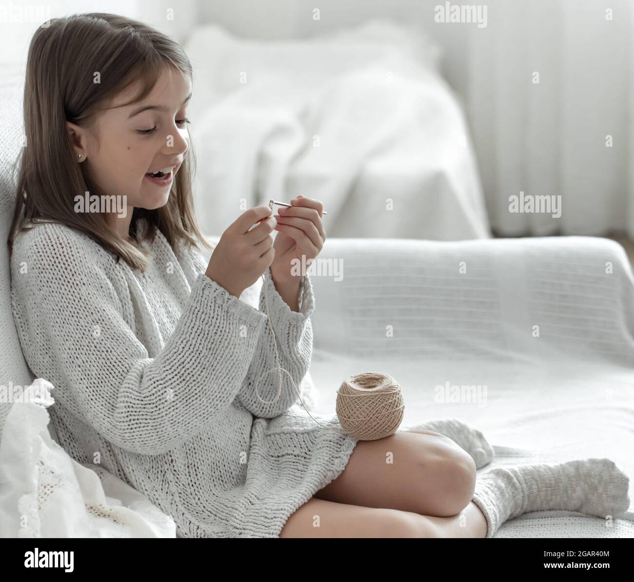 Little girl with a ball of thread and a needle at home on the couch ...