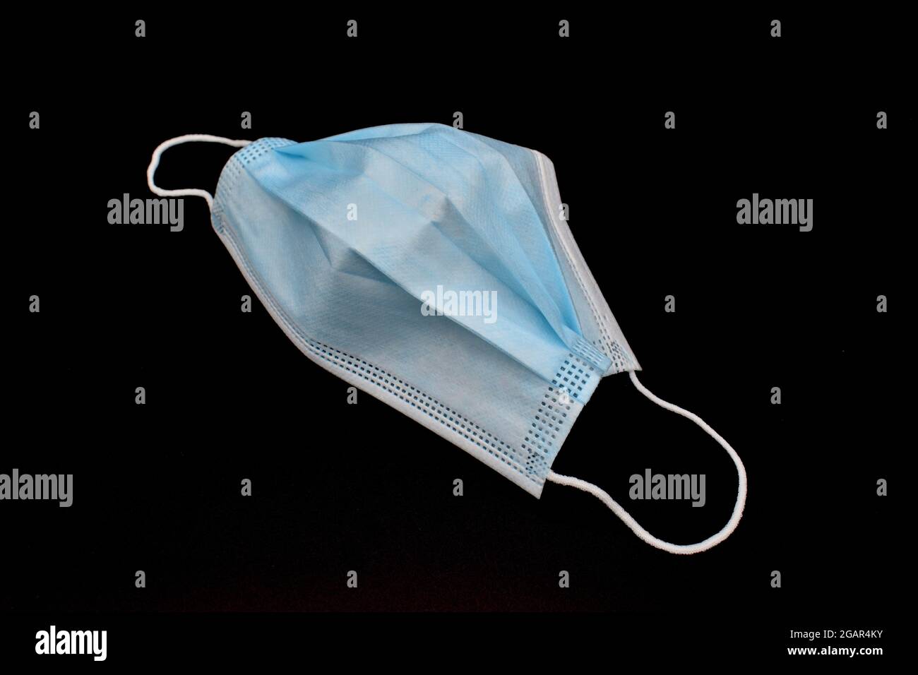 Used disposable surgical mask or blue colored new medical respirator. COVID-19 prevention. H1N1, H5N1 safety measures. Isolated on black background. Stock Photo
