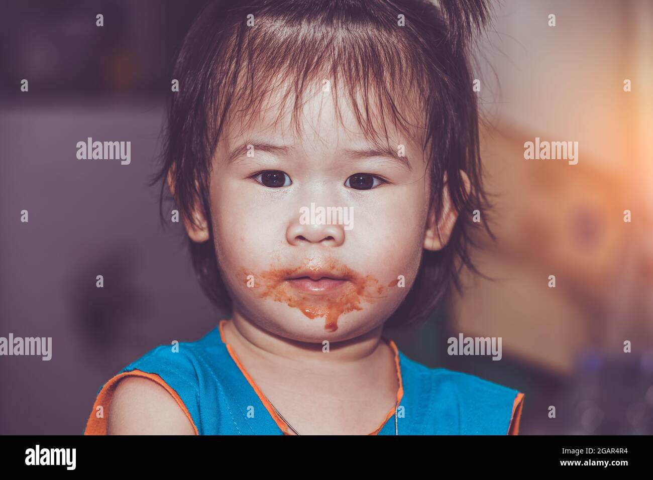 Portrait of a asian child enjoy eating. Her mouth get stained with ketchup. Charming girl playing with food and learning to eat. Dirty face of happy k Stock Photo