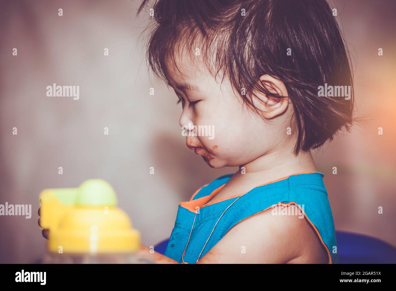 Side view. Asian child enjoy eating. Her hand and mouth get stained with ketchup. Charming girl playing with food and learning to eat. Dirty face of h Stock Photo