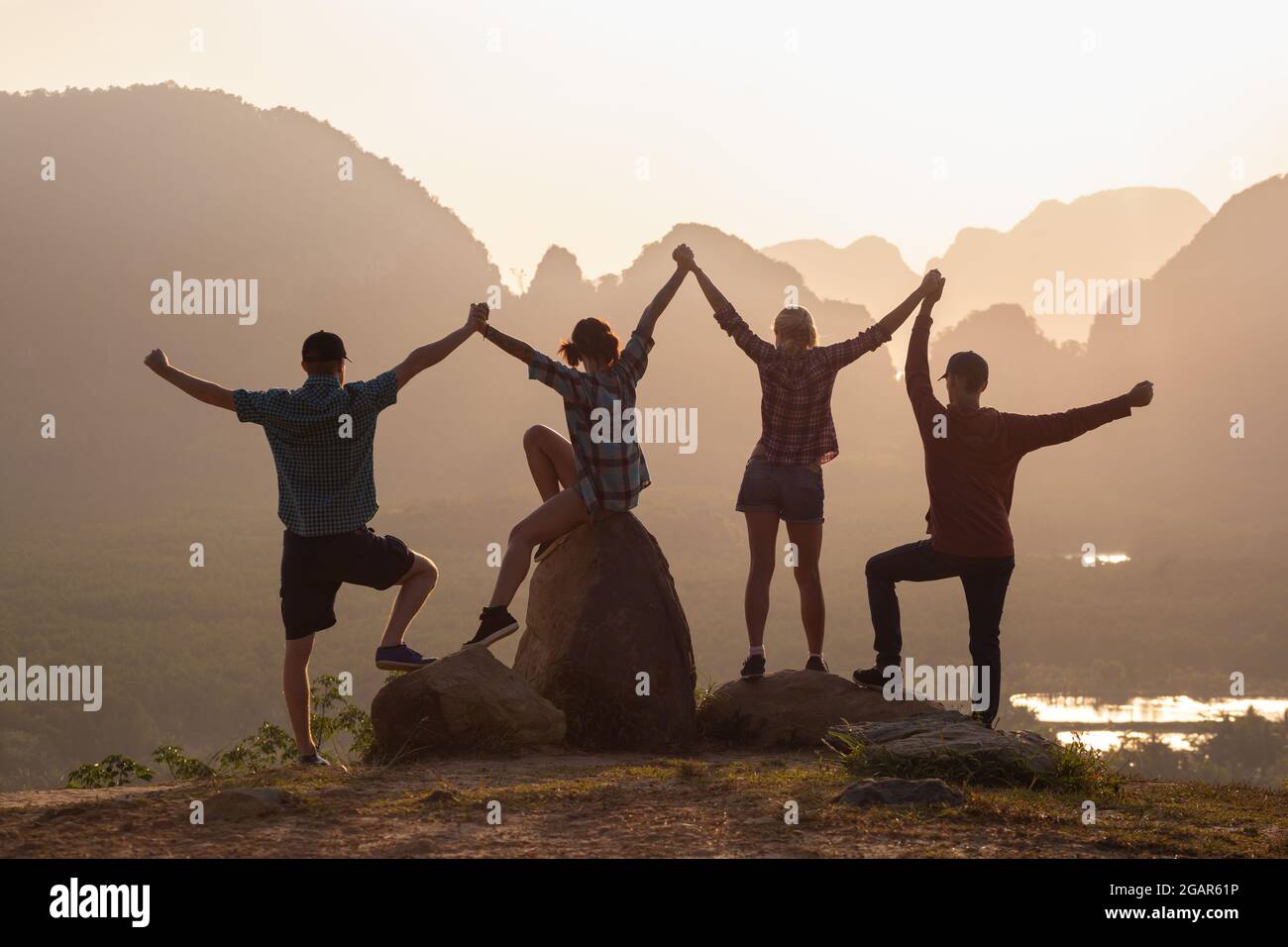 Togetherness concept with four silhouettes of young friends standing against sunrise and mountains Stock Photo