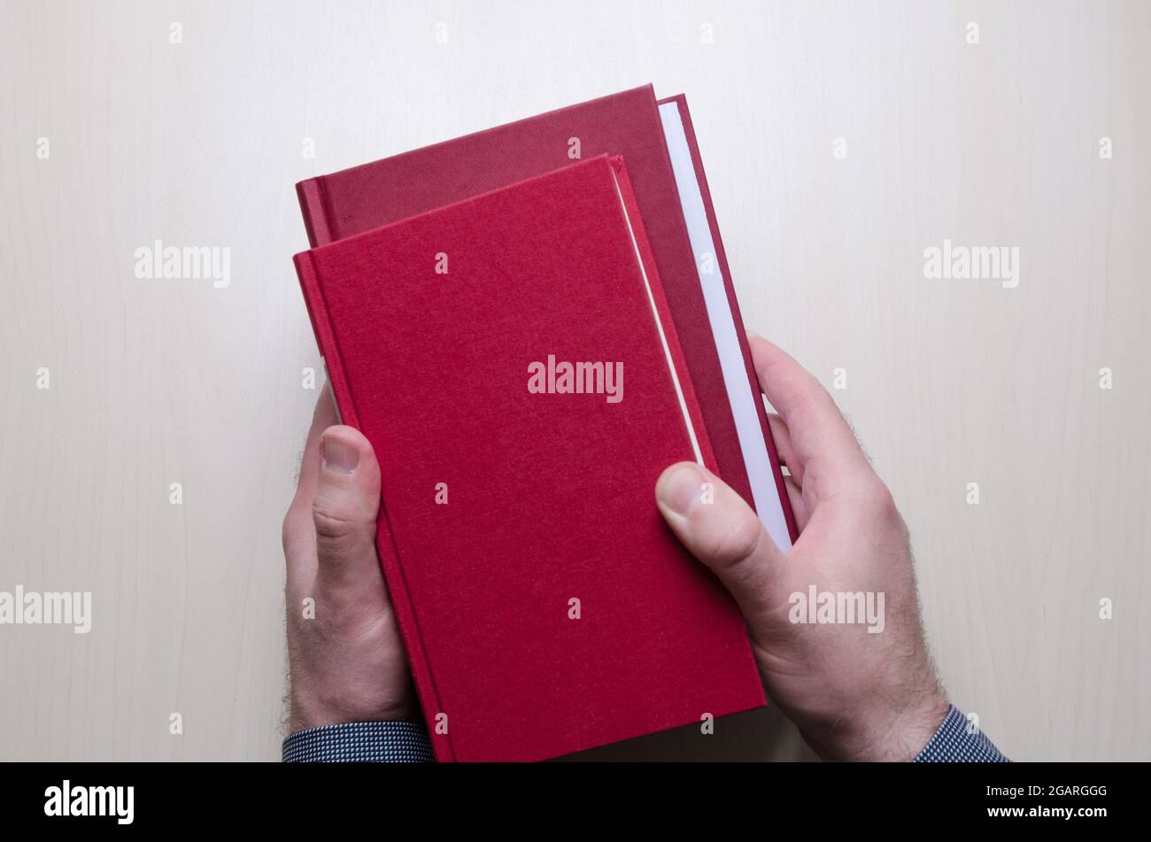 Hand holding two red hardcover books or bible above wooden table or desk in both hands, indoors, literature, library concept Stock Photo