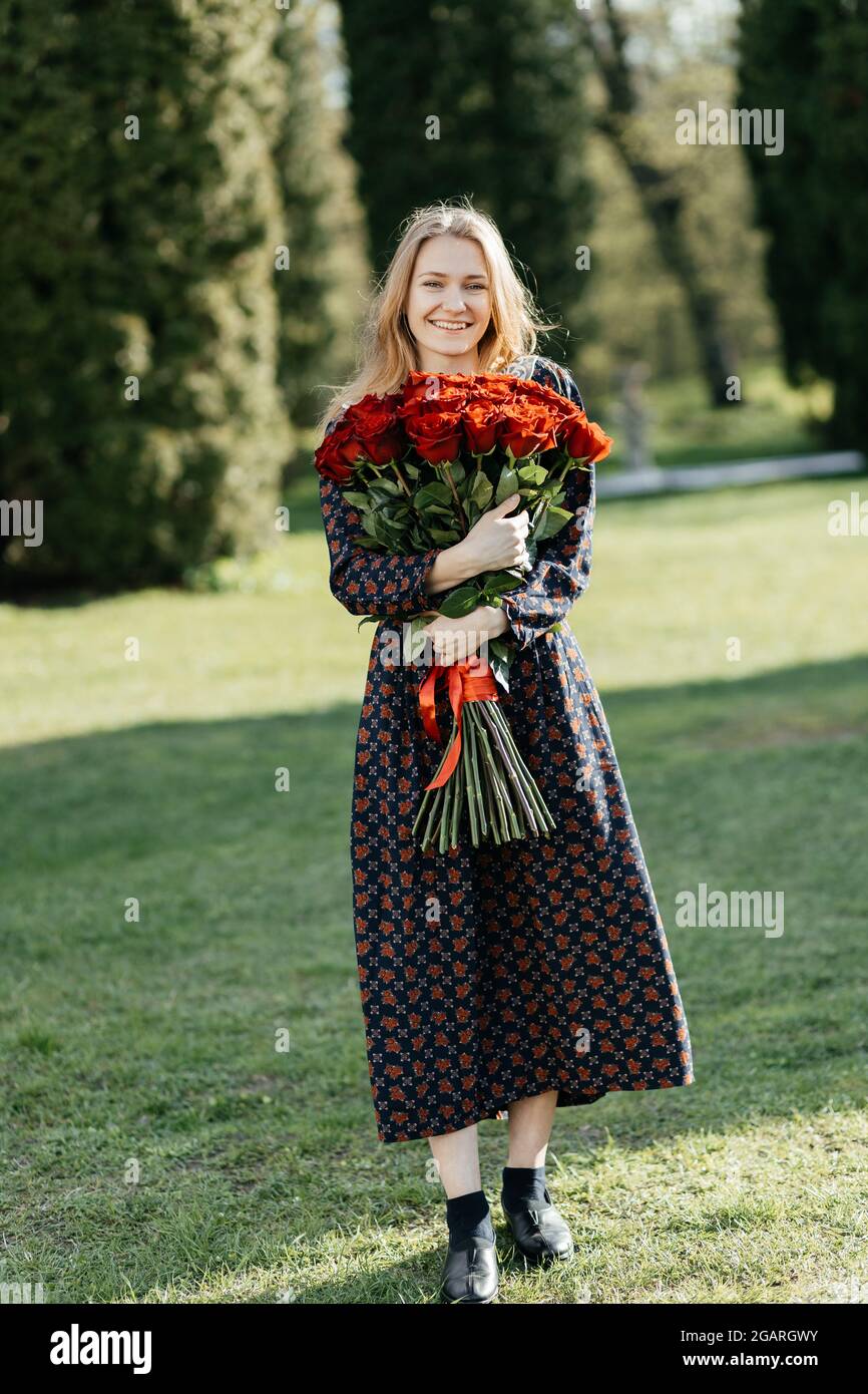 Young girl standing on the lawn smiling and looking at the camera with a bouquet of red roses Stock Photo