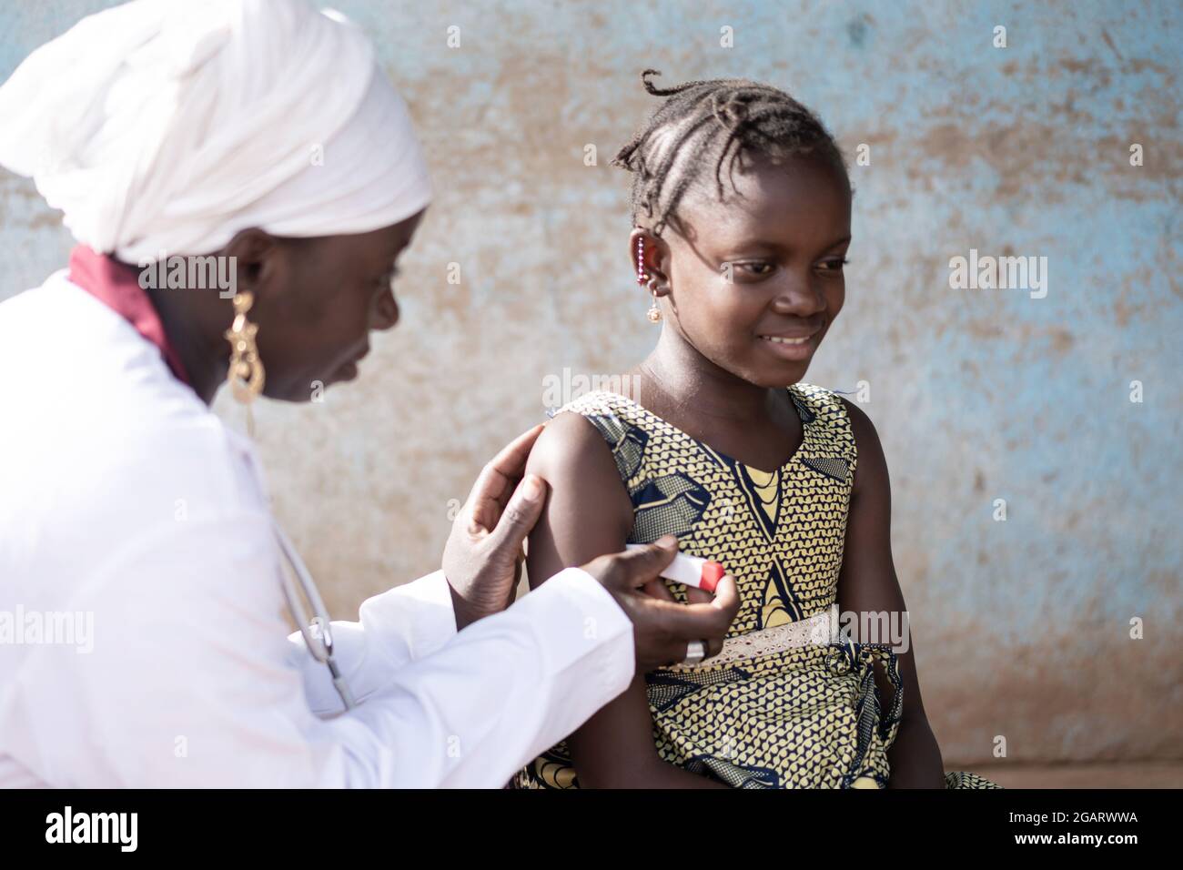 In this closeup, a gentle black nurse is measuring the axillary temperature of a smiling little African girl Stock Photo
