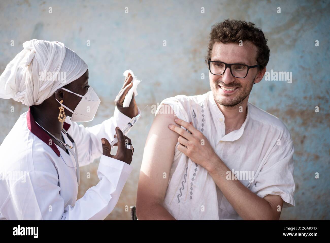 IN this image, a black nurse wearing a protective mask, with syringe and gauge in her hands is preparing to inject a booster dose of vaccine in the ar Stock Photo