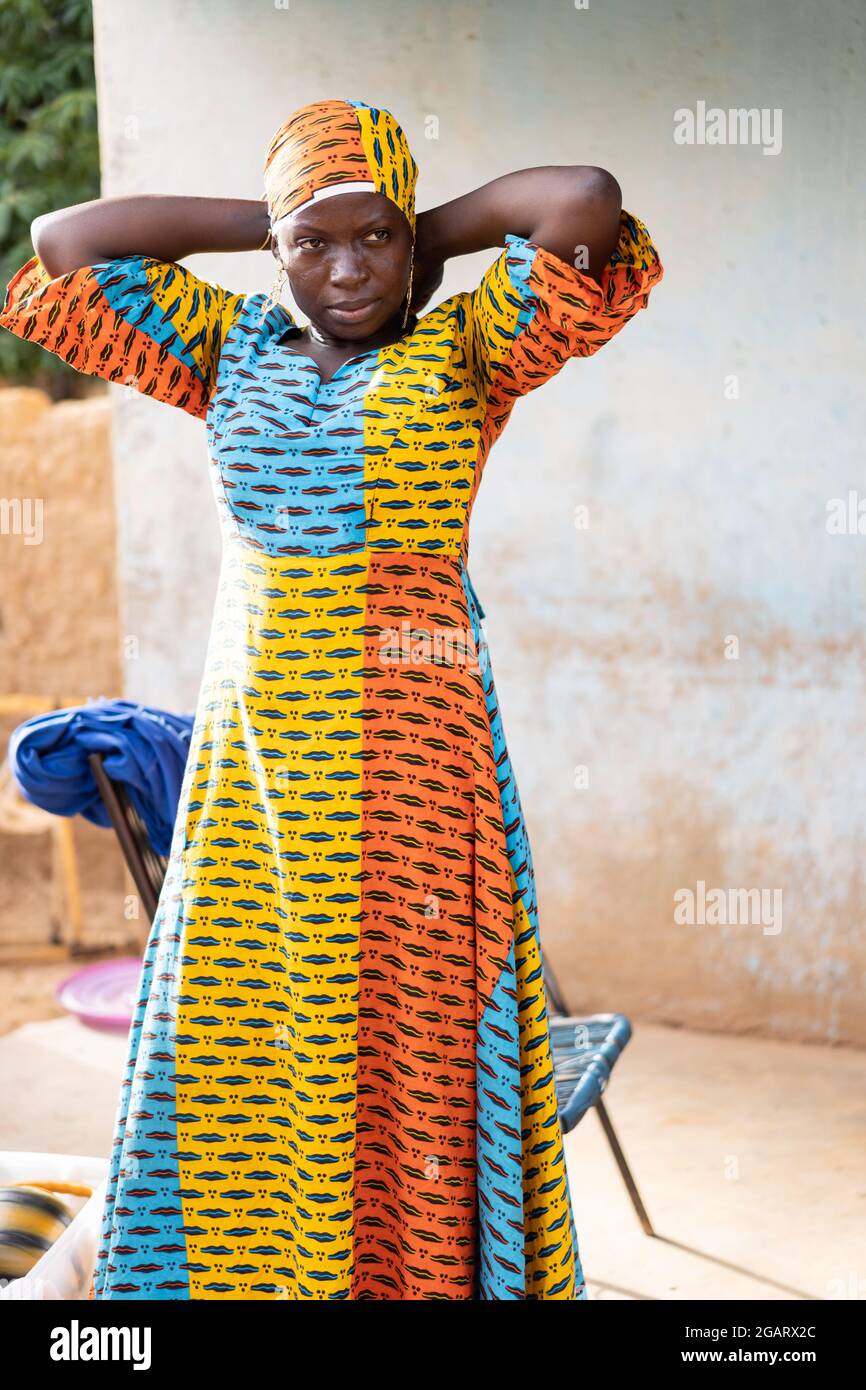 In this image, a tall young black housewife wearing a colourful traditional  African long dress is fixing her matching headscarf Stock Photo - Alamy