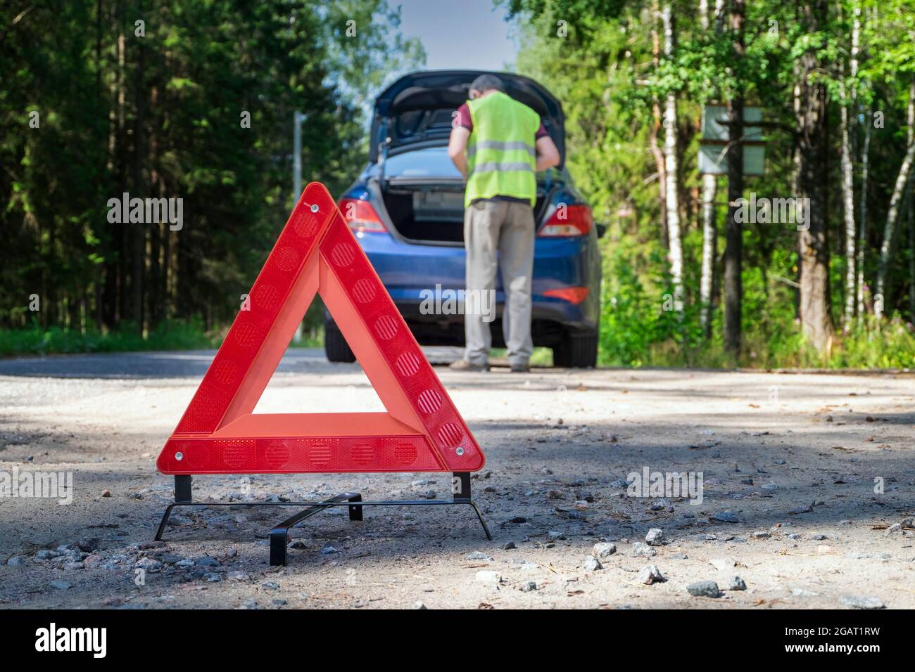 Red warning sign stands on the side of road next to damaged vehicle ...