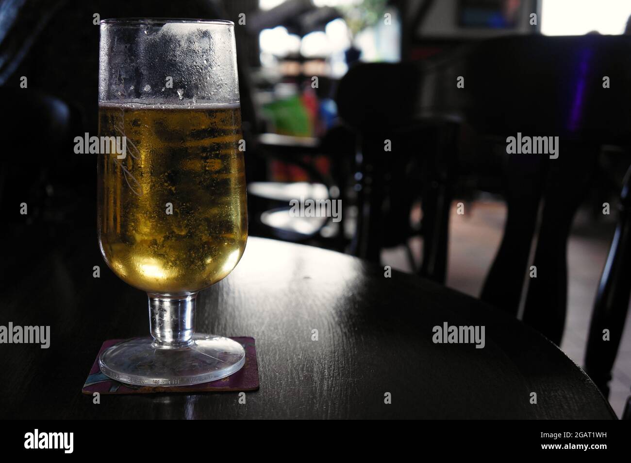 A part filled pint of beer on a pub table with a naturally lit, soft focused  background Stock Photo