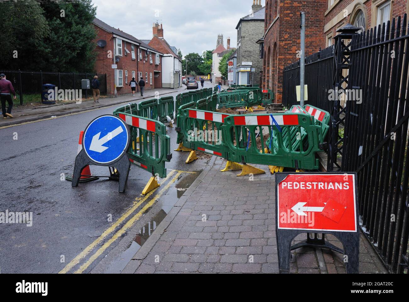 Road works with green barriers diverting pedestrians around a hole in the pavement on the High street Stock Photo
