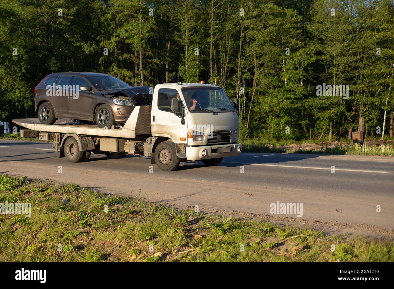 A tow truck is driving a car after an accident. Car transportation on a cargo platform. The loader takes away the emergency vehicle. Stock Photo