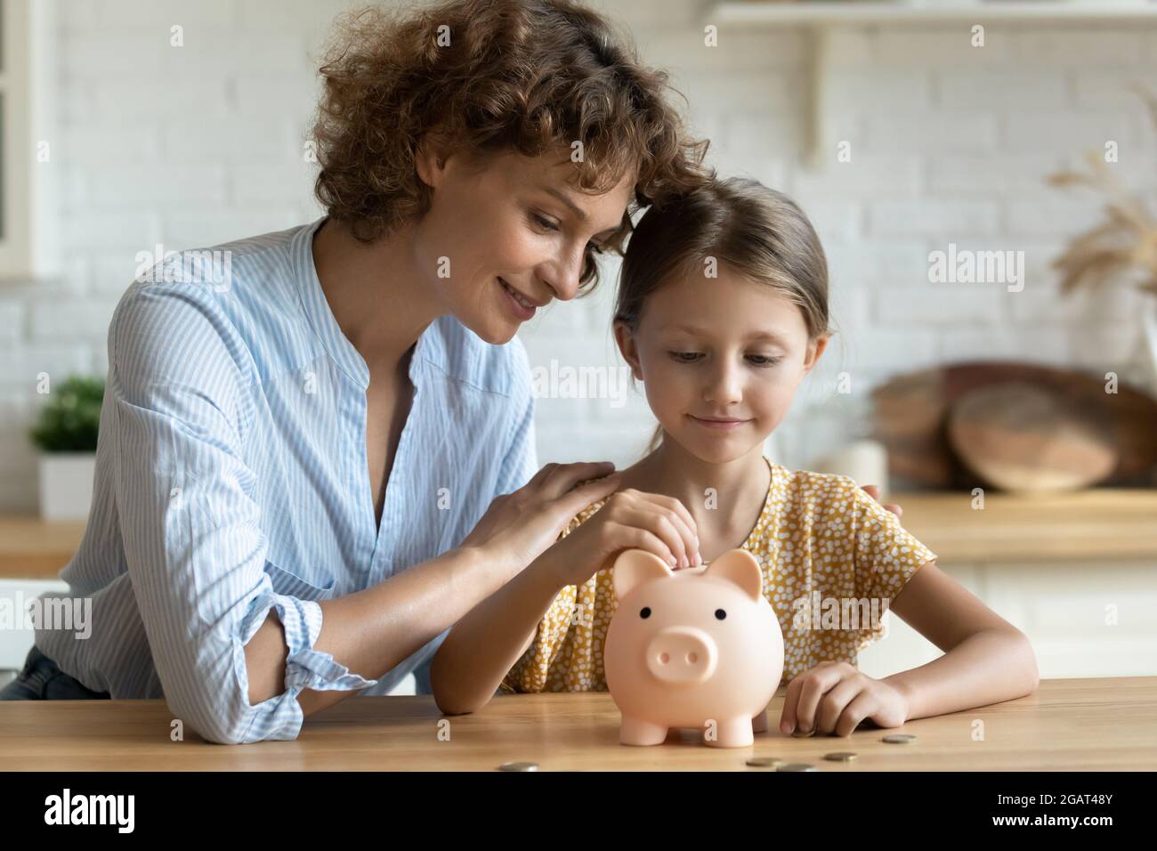 Little girl with mother putting coin into pink piggy bank Stock Photo ...