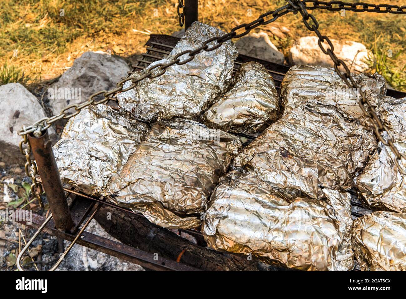 https://c8.alamy.com/comp/2GAT5CX/meat-grilled-in-foil-on-flaming-bbq-grill-barbecue-cooking-flaming-grill-grid-food-background-in-aluminum-foil-portrait-of-the-cooking-food-with-alu-2GAT5CX.jpg