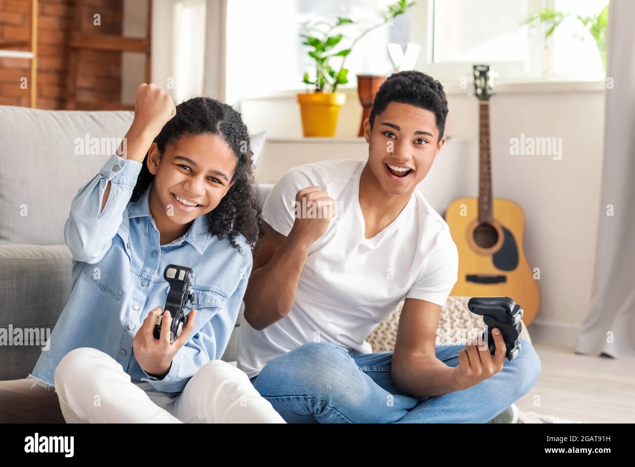 AfricanAmerican brother and sister playing video game at home Stock