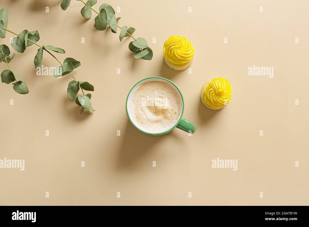 Cup of coffee with cupcakes and plant branches on color background Stock Photo