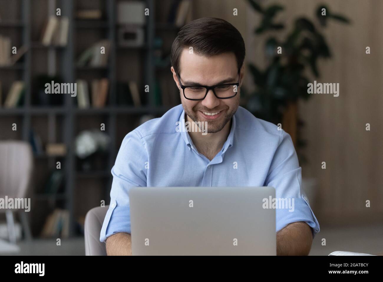 Smiling young male worker use computer type document at desk Stock Photo