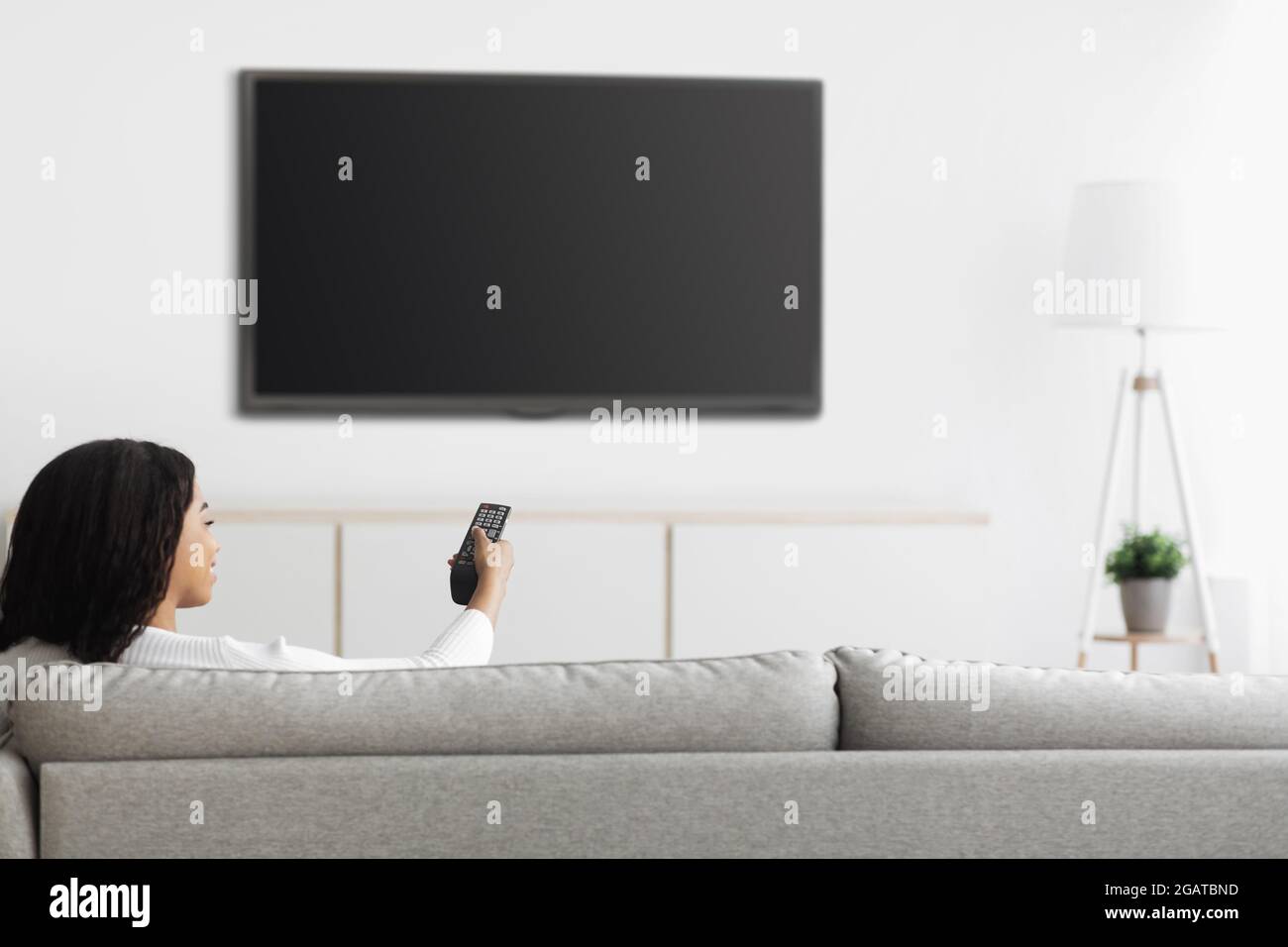 African american woman watching TV pointing remote control at flatscreen plasma television set with blank screen, switching channels while sitting on Stock Photo
