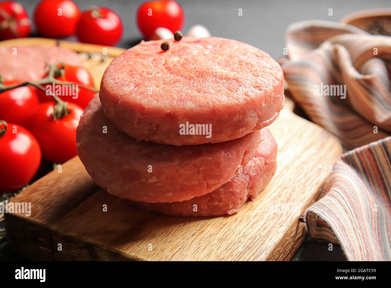 Wooden board with raw cutlets made of fresh forcemeat on dark