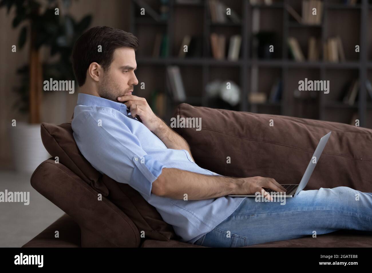 Serious young man sit on sofa engaged in computer work Stock Photo