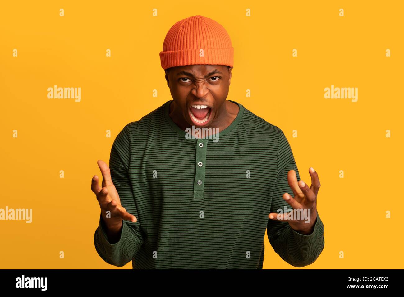 Portrait of furious african american guy shouting with rage at camera, very angry black man raising hands and screaming with fury while standing isola Stock Photo