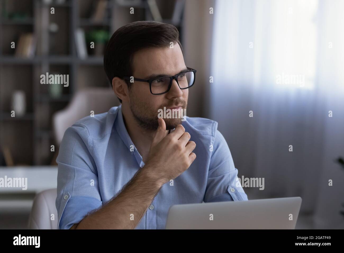 Pensive young man work at laptop online look aside think Stock Photo