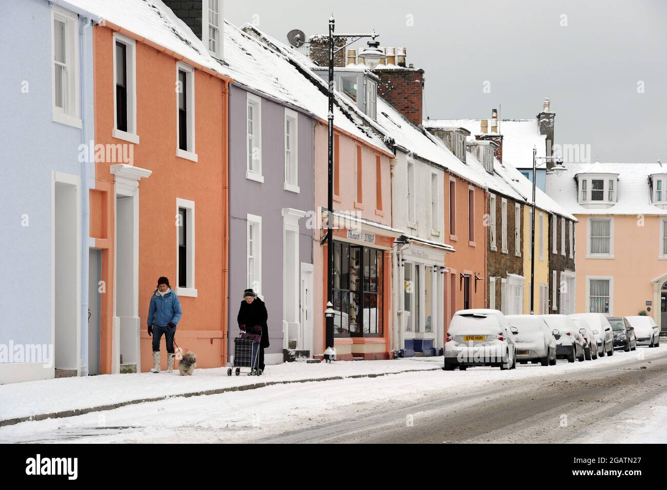 A street in Kirkcudbright, Dumfies and Galloway, Scotland. The houses are colourful and winter snow is on the road and pavement Stock Photo