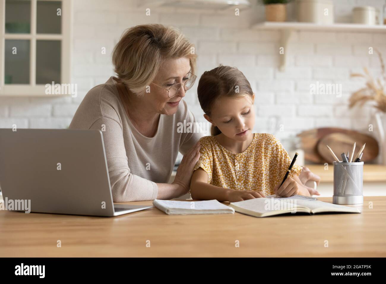 Caring grandmother in glasses helping little granddaughter with school homework Stock Photo