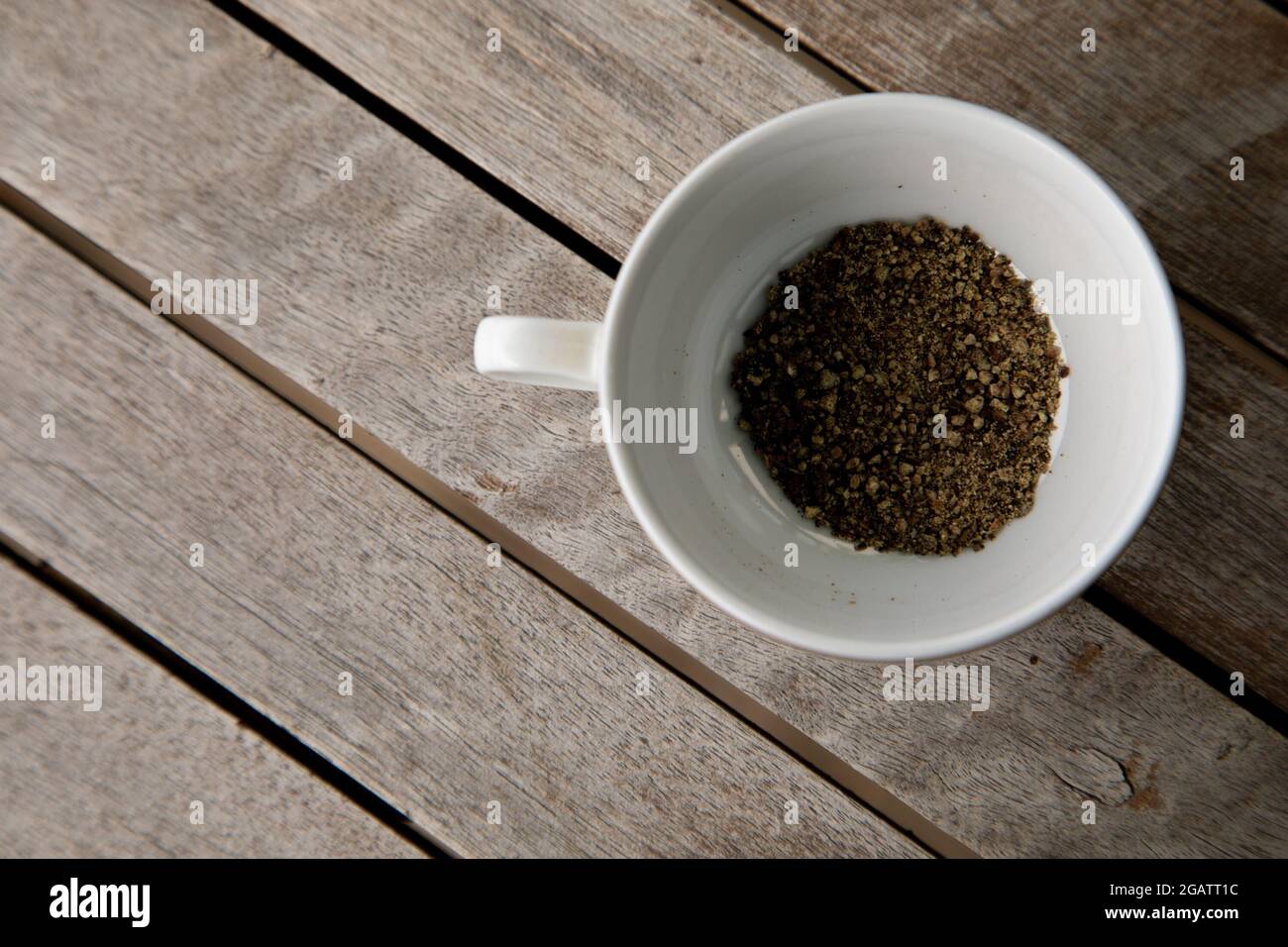 Cracked black pepper in a coffee cup on a wooden table Stock Photo