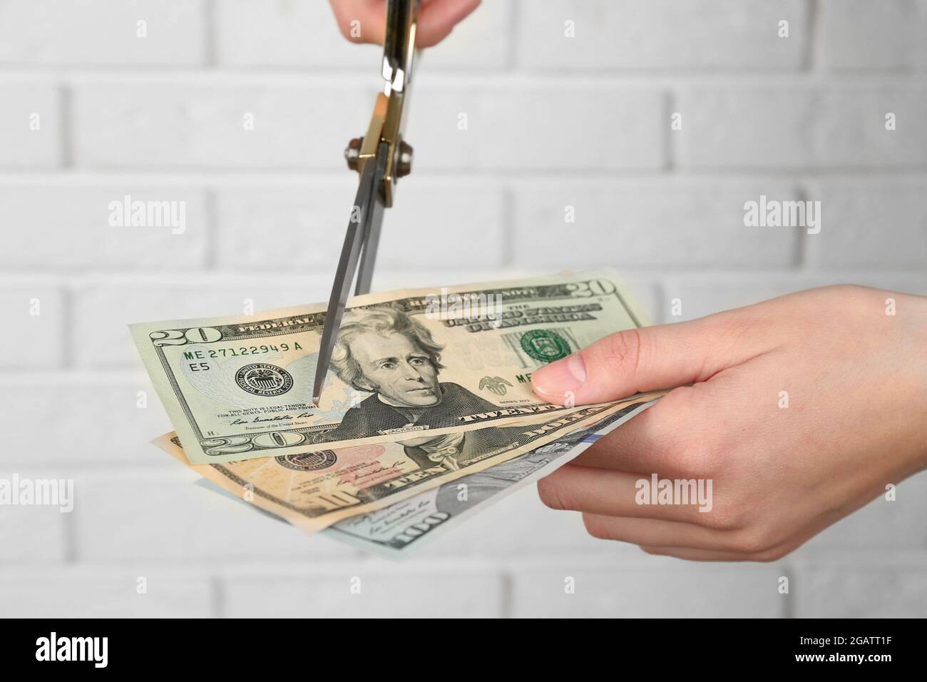Hands with scissors cutting money on white brick wall background Stock