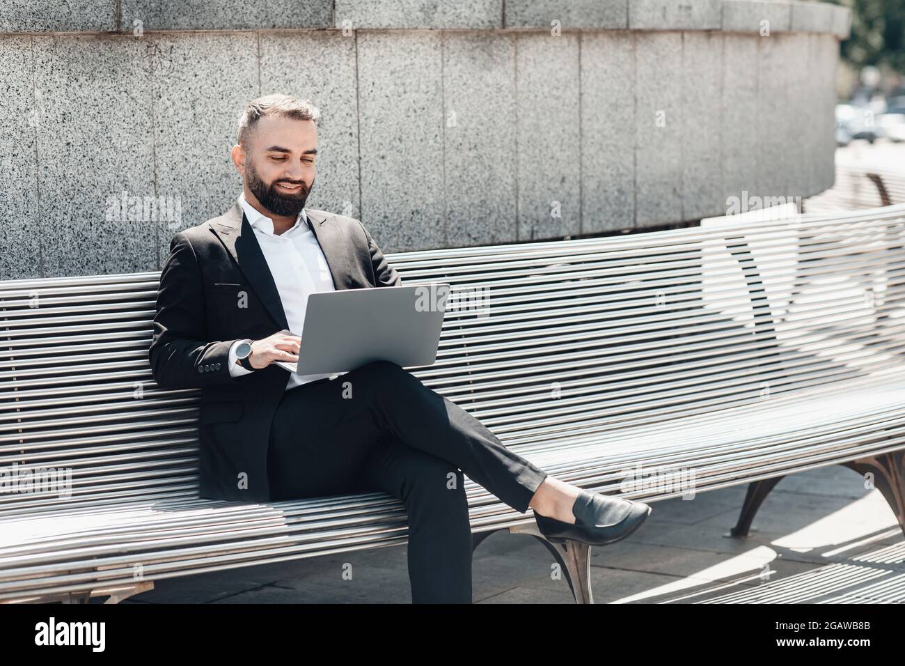 Remote work during covid-19 lockdown outdoors. Confident mature businessman or manager in suit using laptop while sitting on bench near office center Stock Photo