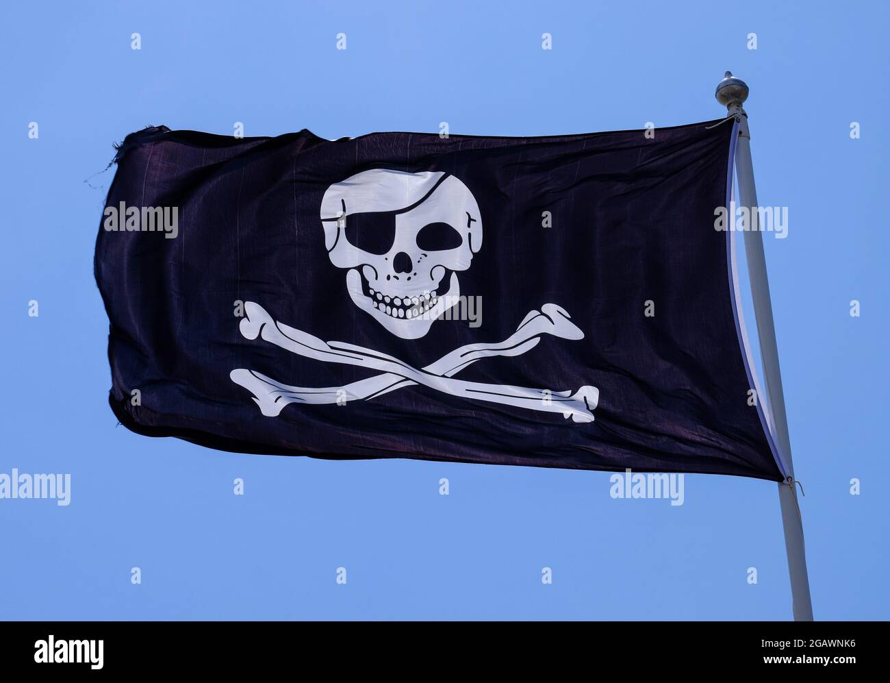 Pirate flag also known as a Jolly Roger flag or a Skull and Cross Bones Flag, pictured against a blue sky. Stock Photo