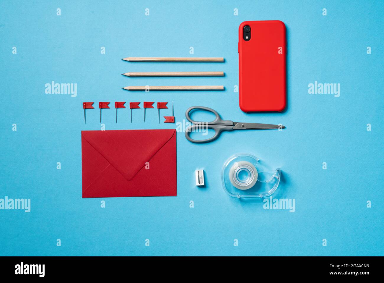 The set of a red phone, an envelope, a scissors, a sharpeners, a pencils and a scotch tape lying in a blue studio Stock Photo