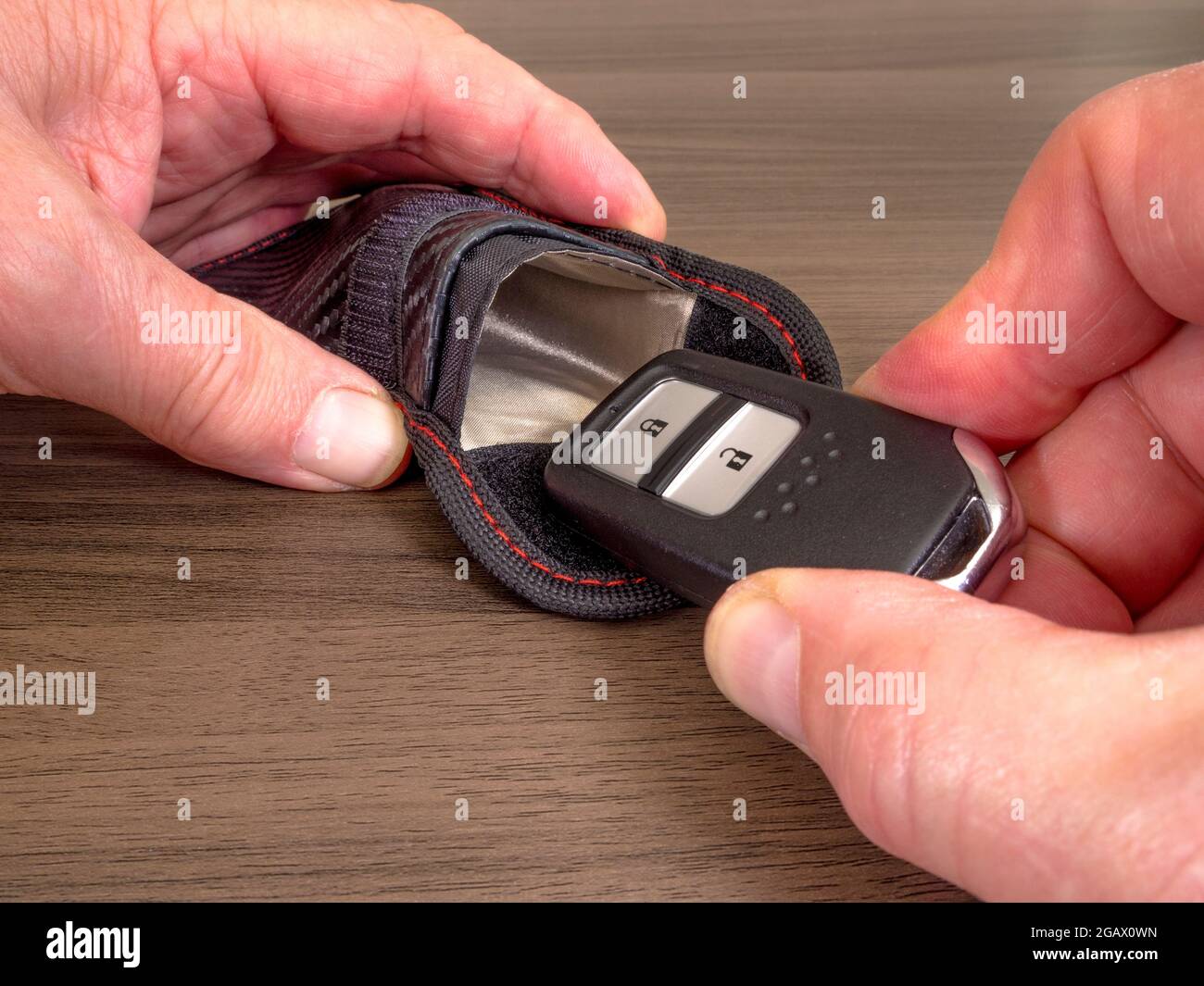 Closeup of a man’s hands sliding a keyless fob in our out of a radio signal-blocking / Faraday pouch, to prevent unauthorized access to a vehicle. Stock Photo