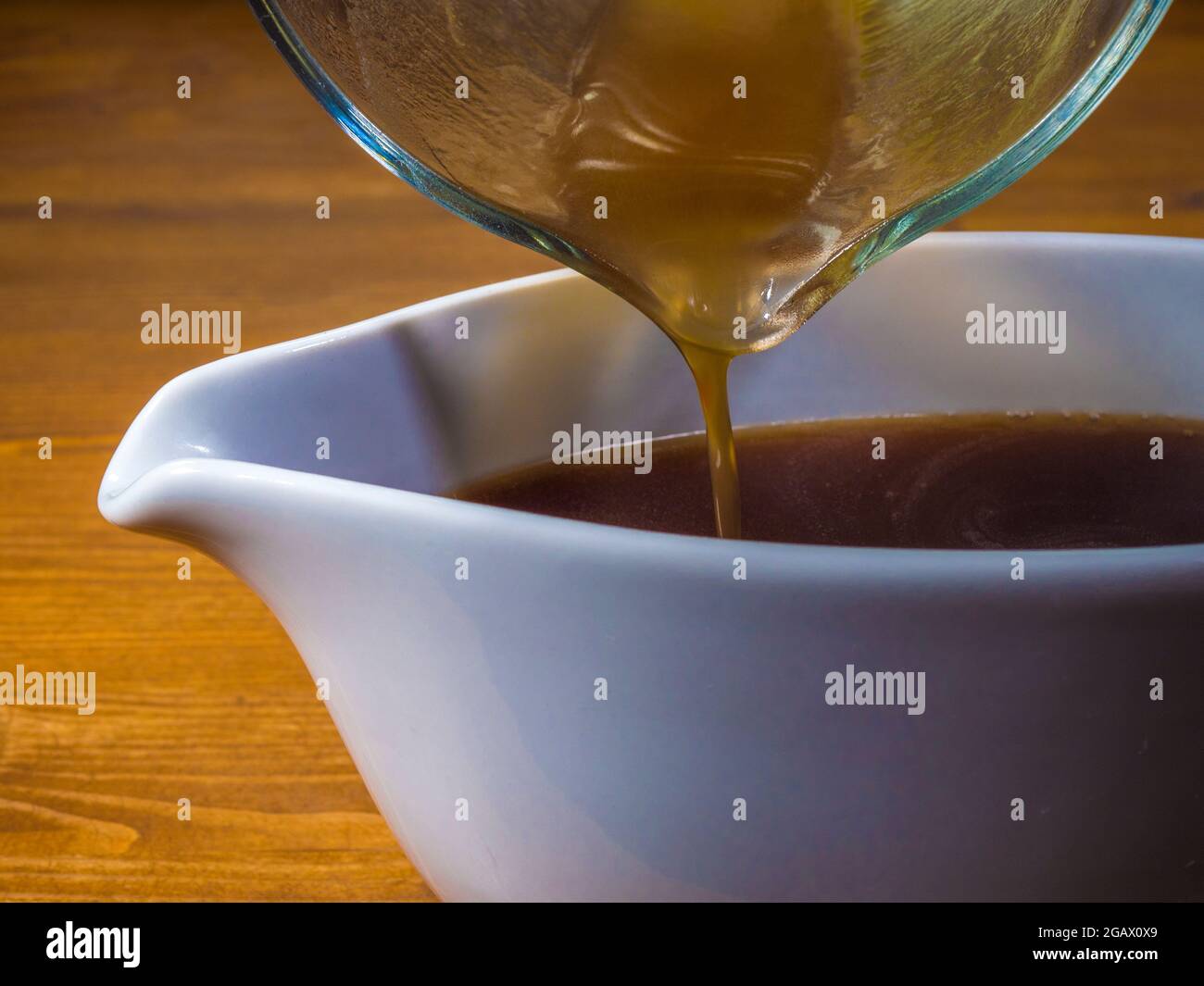 Closeup POV shot of hot gravy finishing being poured from a glass measuring jug into a serving boat. Stock Photo