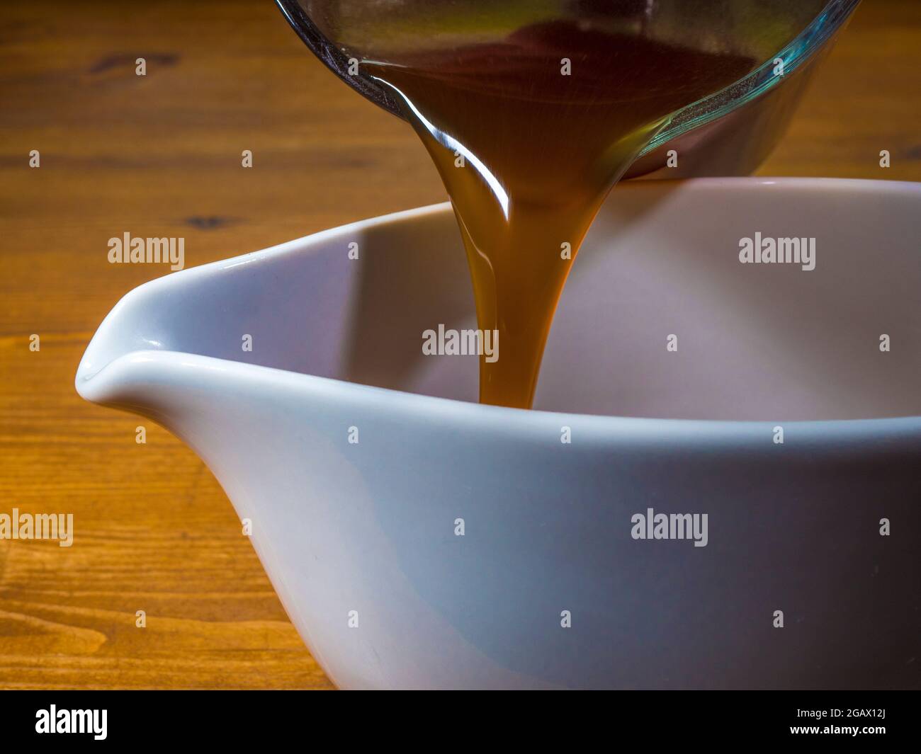 Closeup POV shot of hot gravy strarting to be poured from a glass measuring jug into a serving boat. Stock Photo