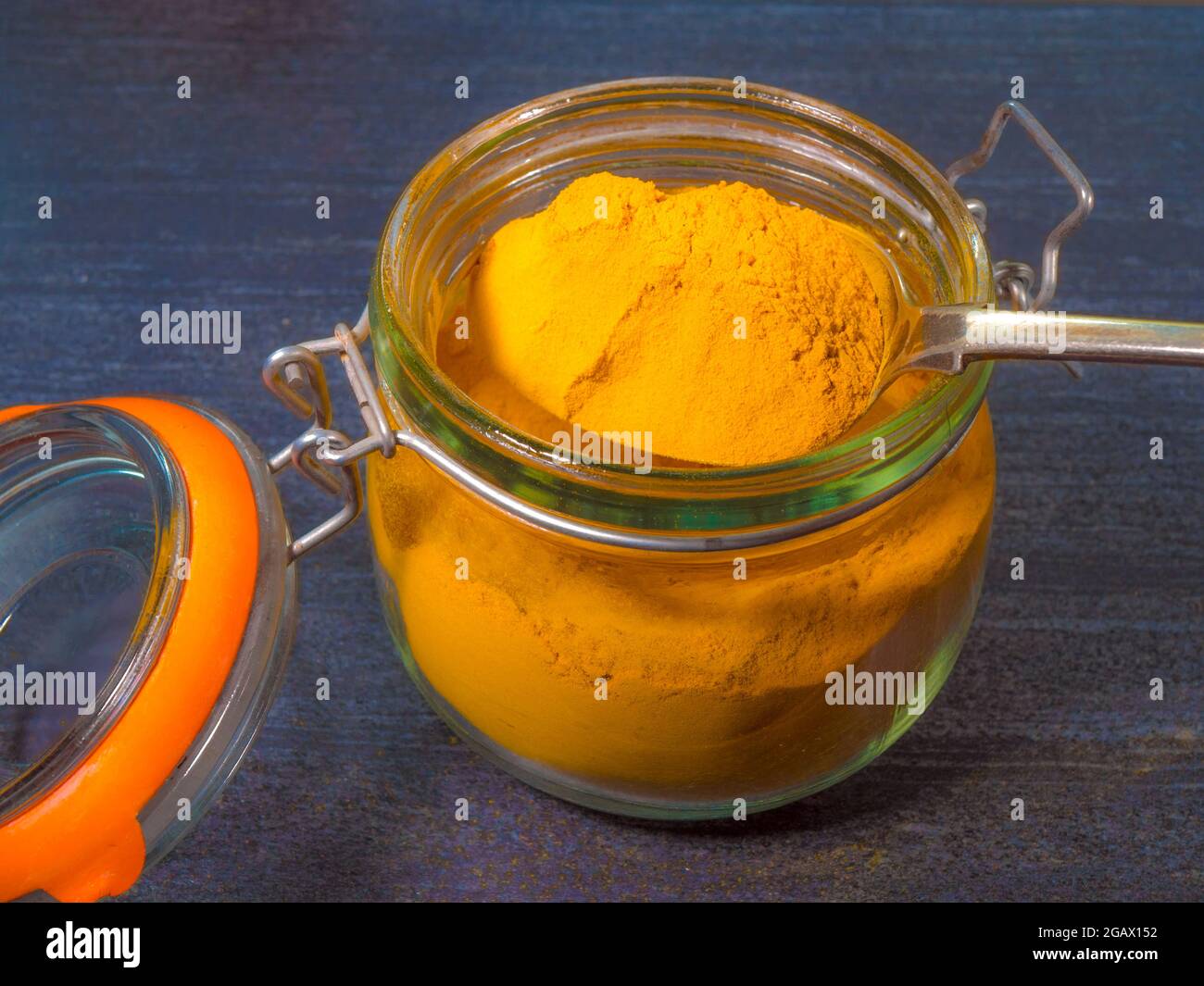 Closeup POV shot of a large spoonful of dry ground turmeric being lifted from a glass storage jar. Stock Photo