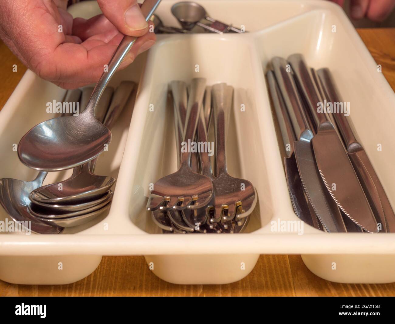 Closeup POV shot of a man’s hand placing a spoon on top of others in a plastic cutlery tray, with compartments for steel knives, forks and spoons. Stock Photo