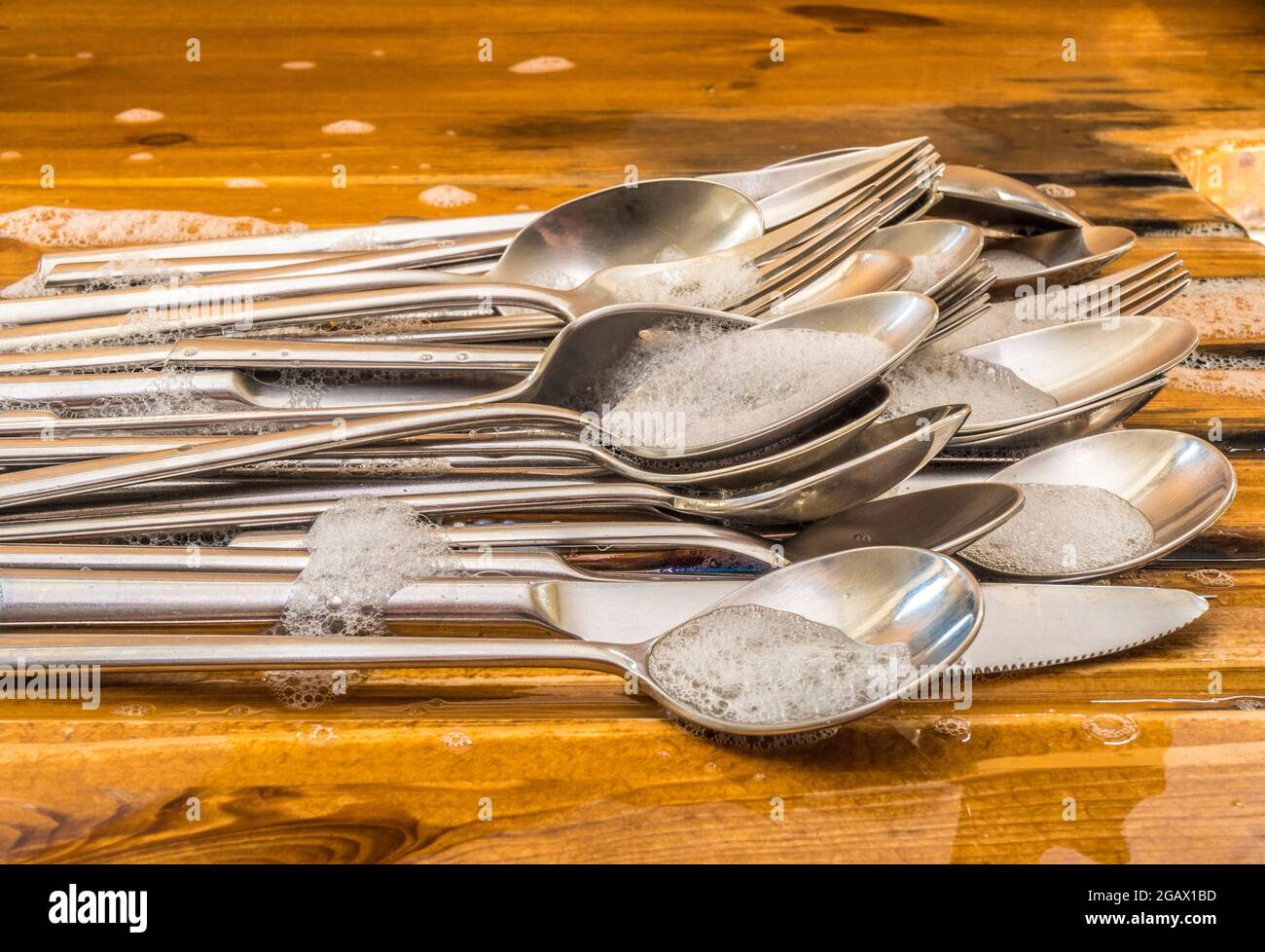 Closeup POV shot of soapy washed steel cutlery plled up on a wooden sink draining board. Stock Photo