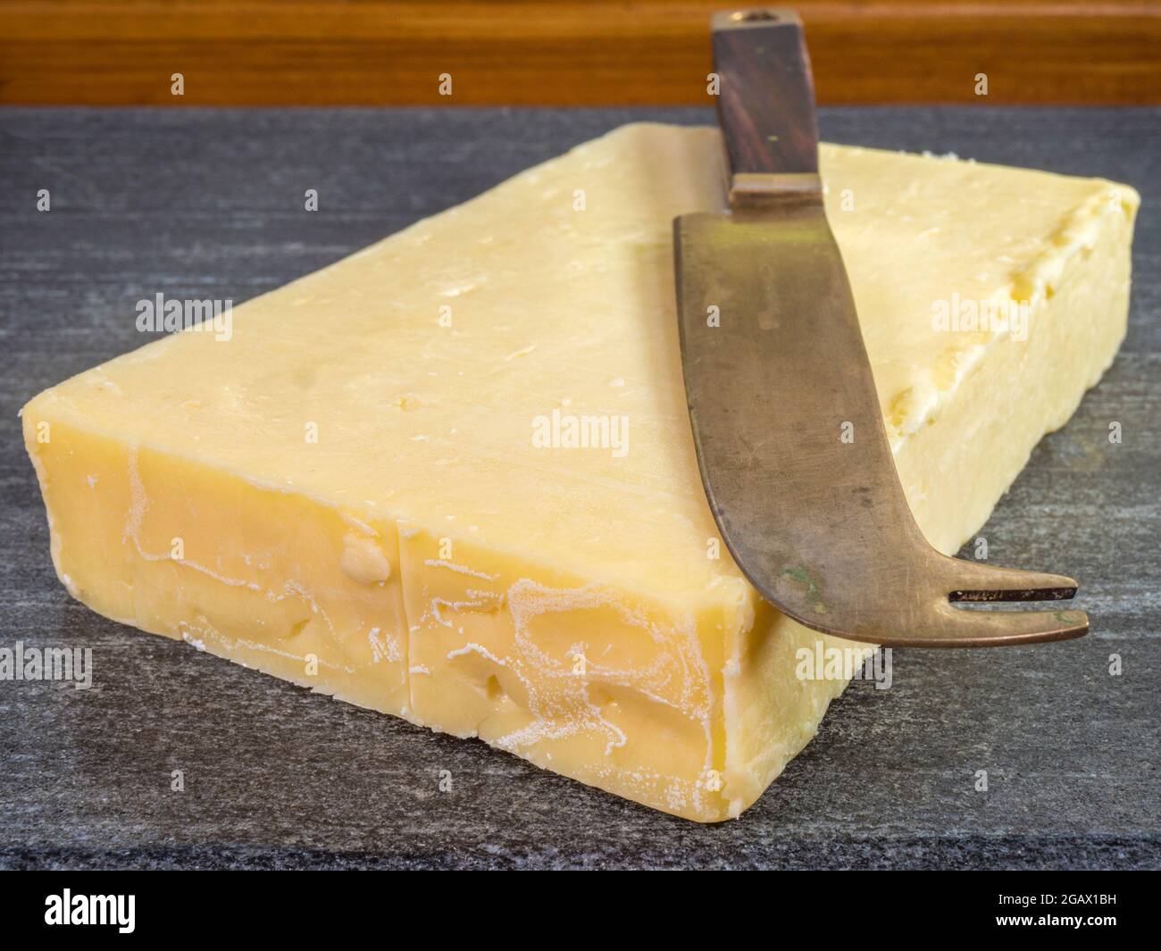 Closeup POV shot of a marble board with a thick oblong slab of fresh cheddar, with a cheese knife on top. Stock Photo