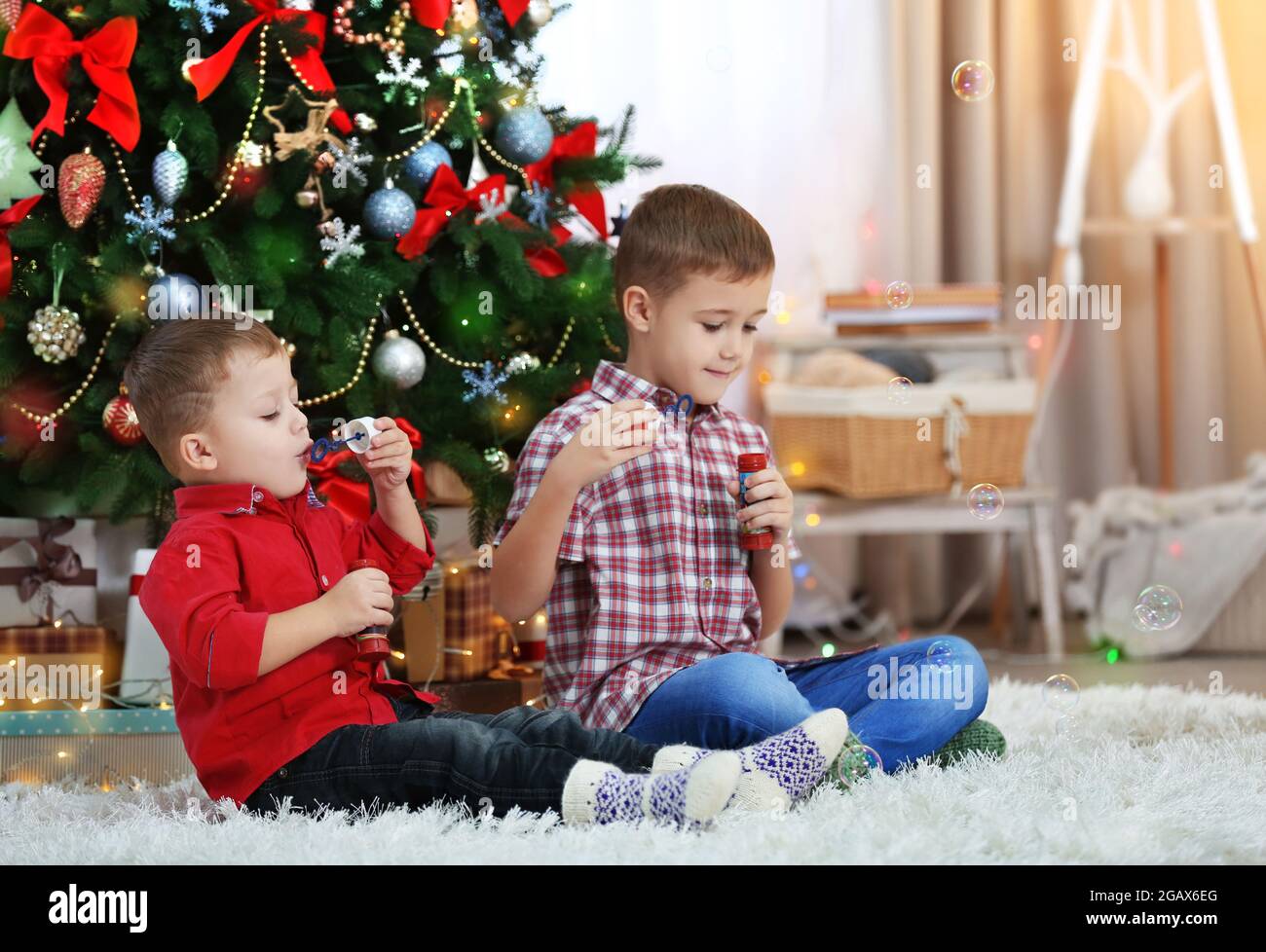 Two cute small brothers blows soap bubbles on Christmas tree background ...