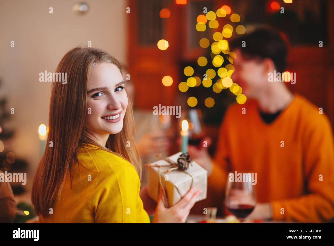 Happy smiling blond woman giving wrapped gift to friend while sitting at table and celebrating Christmas together Stock Photo