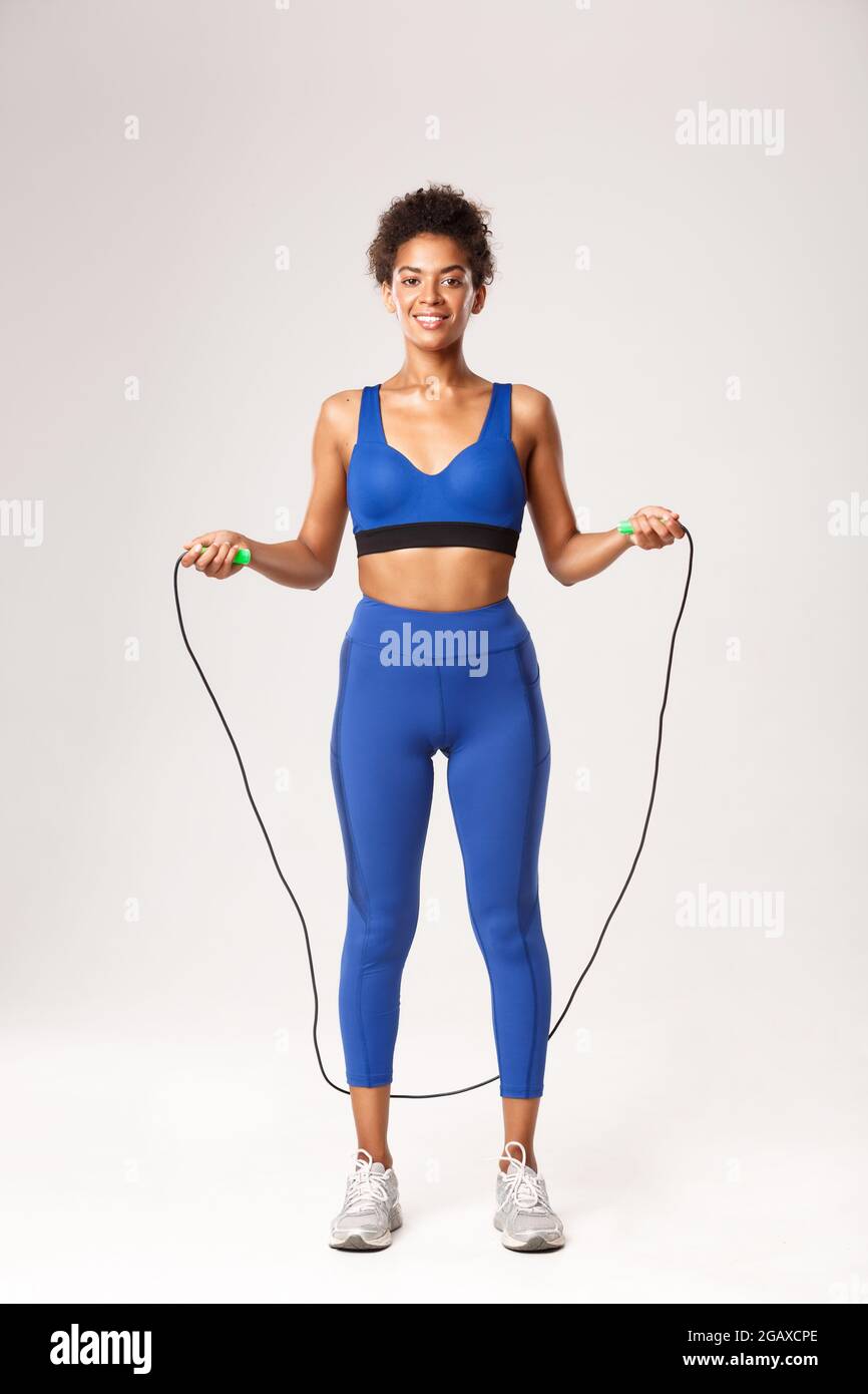 Full length of strong female athlete in blue sport outfit, jumping with  skipping rope and smiling, doing exercises against white background Stock  Photo - Alamy