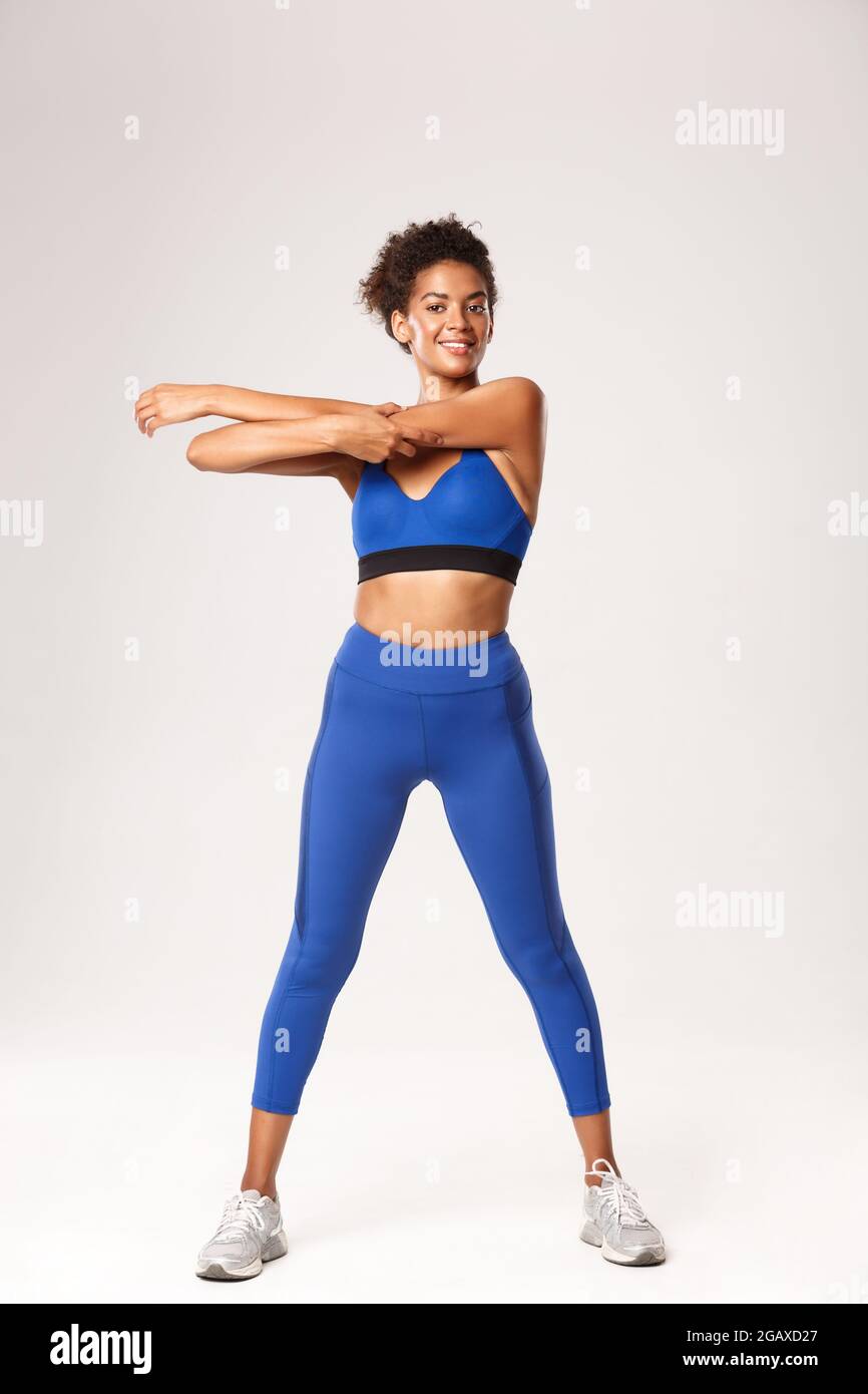 Full length of smiling athletic african-american sportswoman, wearing blue sport  outfit, stretching before fitness activity, workout over white Stock Photo  - Alamy